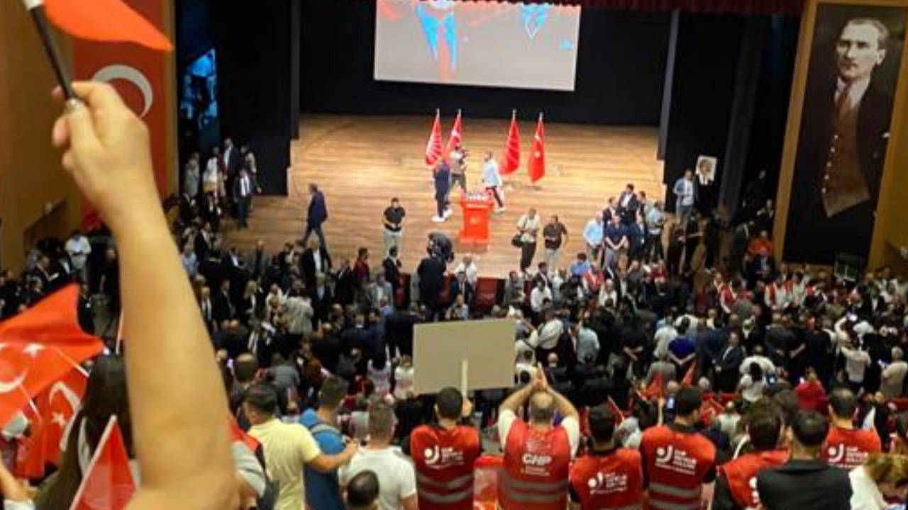 CHP kongre salonunda Türk bayrakları ve kırmızı yeleklilerle dolu kalabalık, sahnede parti bayrakları ve Atatürk portresi